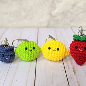 May include: Four crocheted fruit keyrings: a blueberry, lime, lemon, and strawberry. Each fruit has a smiling face and a silver keyring clasp. The strawberry has a green leafy top.