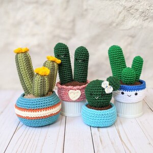 May include: A collection of handmade crochet cactus plants in various sizes and colors. The cacti are in blue, pink, and white pots with smiling faces. Some have yellow flower accents, creating a whimsical and charming display.
