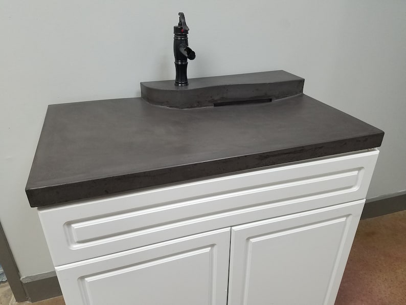 Op de afbeelding: Een moderne badkamermeubel met een donkergrijze aanrecht en een zwarte kraan. De wastafel heeft een witte kast met twee deuren en een verzonken paneelontwerp. De kraan is een zwanenhalsmodel.