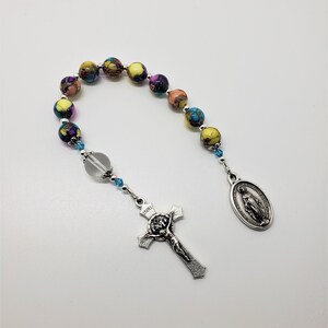 May include: A colorful beaded rosary with a silver crucifix and a silver oval pendant featuring the image of the Virgin Mary. The beads are multi-colored with shades of yellow, orange, purple, and blue.