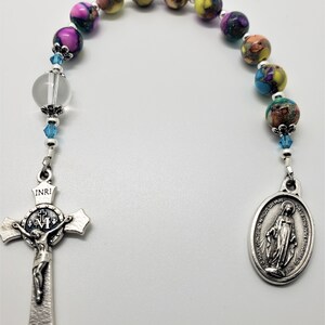 May include: A colorful rosary with a silver crucifix and a silver medal of the Virgin Mary. The beads are made of glass and have a variety of colors, including yellow, blue, pink, and green. The crucifix has the inscription "INRI" on the top and a depiction of Jesus Christ on the cross. The medal has the inscription "O Mary conceived without sin, pray for us who have recourse to thee" on the back.