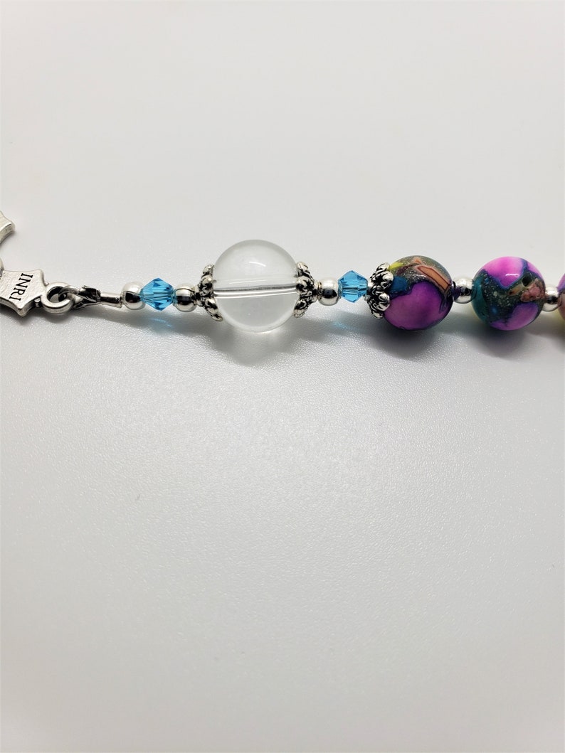 May include: A close-up of a beaded bracelet with a clear crystal bead, blue crystal beads, and pink and green patterned beads.