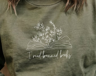 May include: A green sweatshirt with a white outline of a book with flowers growing out of it. The text "I read banned books" is printed below the book.
