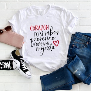 May include: White t-shirt with the text "CORAZÓN TÚ SÍ sabes quererme COMO A MÍ ME gusta" in black with a red heart.