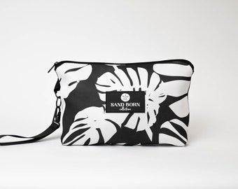May include: Black and white zippered pouch with a tropical leaf print and a black strap. The pouch has a logo that says "SAND BORN collection".