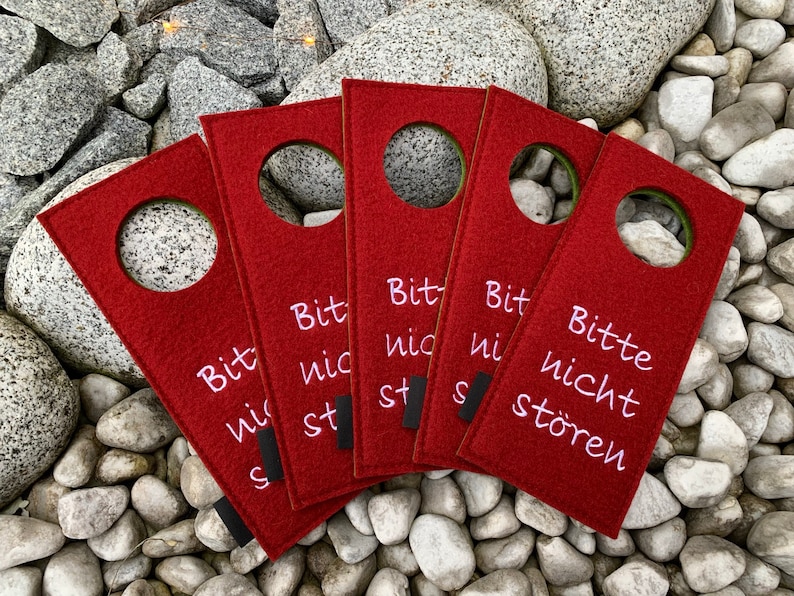 May include: Five red felt door hangers with a white circle in the center and the text "Bitte nicht st&ouml;ren" in pink lettering. The text translates to "Please do not disturb".