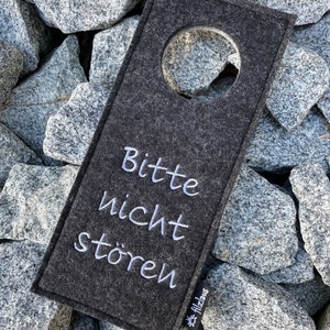 May include: A gray felt door hanger with a white circle cutout and the text "Bitte nicht st&ouml;ren" in white embroidery. The text "Filzlaus" is also embroidered in white in the lower right corner.