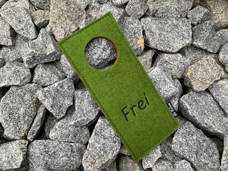 May include: Green felt door hanger with a round hole in the center and the word "Frei" embroidered in black thread.