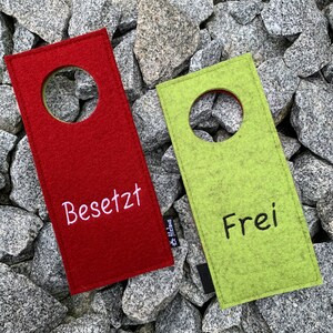 May include: Two felt door hangers, one red and one green, with a hole in the center. The red hanger says "Besetzt" and the green hanger says "Frei".