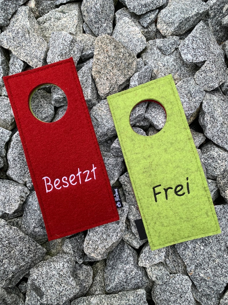 May include: Two felt door hangers, one red and one green, with a hole in the center. The red hanger says "Besetzt" and the green hanger says "Frei".