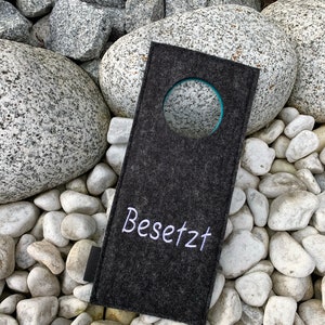 May include: A gray felt door hanger with a white circle and the word "Besetzt" embroidered in white.
