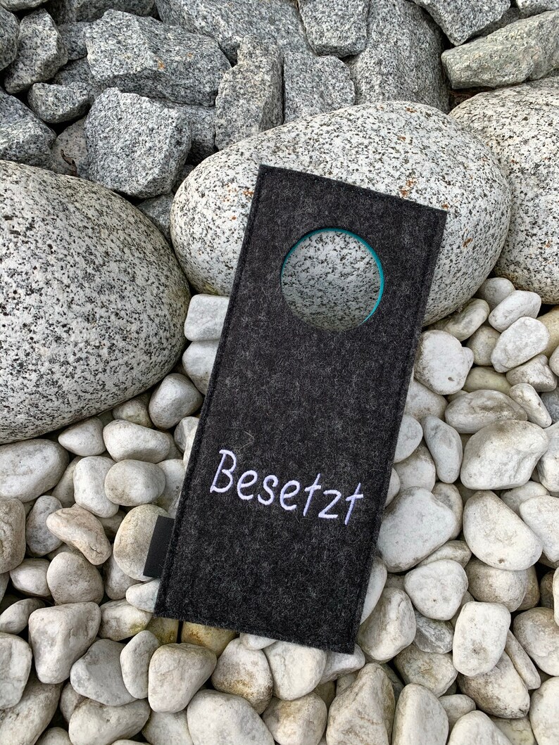 May include: A gray felt door hanger with a white circle and the word "Besetzt" embroidered in white.