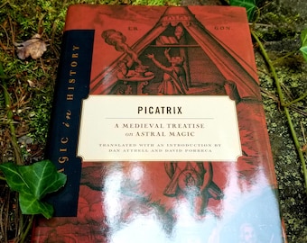 Puede incluir: Un libro de tapa dura rojo con un título dorado, "Picatrix: A Medieval Treatise on Astral Magic". La portada presenta una ilustración de una persona con una túnica y un sombrero puntiagudo, de pie en una habitación con una ventana y una mesa. El libro está sobre un lecho de musgo verde.