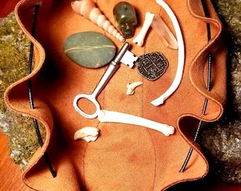 May include: A brown leather pouch with a drawstring closure. The pouch is filled with various items, including a key, a stone, a seashell, a bone, and a small metal charm.