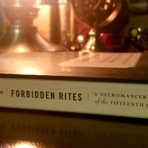 K&ouml;nnte beinhalten: Ein schwarzes Hardcover-Buch mit dem Titel "Verbotene Rituale: Ein Nekromantenhandbuch aus dem 15. Jahrhundert" von Kiechhefer.