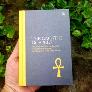 May include: A dark gray book with a yellow spine and the title "The Gnostic Gospels" printed in white. The book includes the Gospel of Judas, the Gospel of Thomas, and the Gospel of Mary Magdalene. A yellow ankh symbol is printed on the front cover.