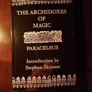 May include: A black book with white text on the cover. The title is "The Archidoxes of Magic" by Paracelsus. The book has an introduction by Stephen Skinner.