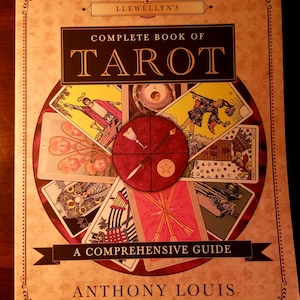 May include: A book titled "Llewellyn's Complete Book of Tarot: A Comprehensive Guide" by Anthony Louis. The cover features a circular design with tarot cards arranged around a central red circle with a five-pointed star.