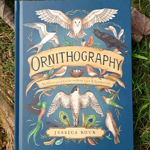 May include: A hardback book titled "Ornithography" with a dark blue cover. The cover features illustrations of various birds, including an owl, hummingbird, and crow. The author's name, Jessica Roux, is also displayed.