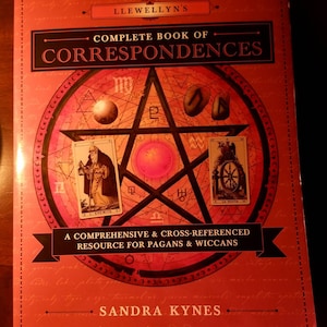May include: A red book with a pentagram and tarot cards on the cover. The title is "Llewellyn's Complete Book of Correspondences". The subtitle is "A Comprehensive & Cross-Referenced Resource for Pagans & Wiccans". The author is Sandra Kynes.
