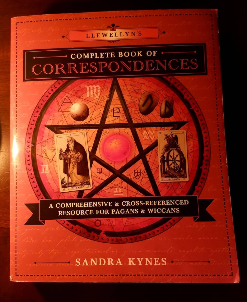 May include: A red book with a pentagram and tarot cards on the cover. The title is "Llewellyn's Complete Book of Correspondences". The subtitle is "A Comprehensive & Cross-Referenced Resource for Pagans & Wiccans". The author is Sandra Kynes.