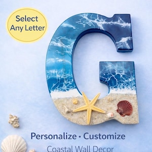 May include: A large letter "G" in shades of blue and white, resembling ocean waves, with a sandy base. Adorned with a starfish and seashells. Text reads "Select Any Letter" and "Personalize • Customize Coastal Wall Decor."