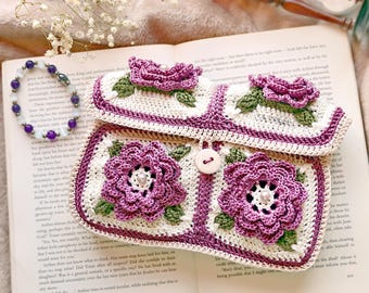 May include: A rectangular crochet pouch featuring a cream-colored base with four prominent purple three-dimensional flowers, green leaves, and a single light-colored button closure. The pouch is accented with purple trim.