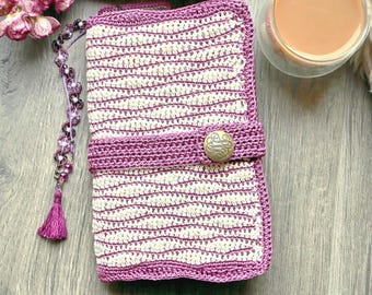 May include: A rectangular crochet book cover featuring alternating wavy stripes of mauve and cream yarn. A horizontal mauve strap secures the cover with a round, metallic gold button. A beaded mauve tassel bookmark hangs from the side.