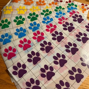 May include: A set of 10 sheets of paw print vinyl decals in various colors, including red, orange, yellow, green, blue, pink, and purple. Each sheet has a grid pattern and multiple paw prints.