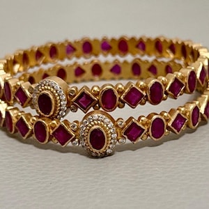 Peut inclure: Deux bracelets en or avec un motif de pierres précieuses roses alternées et de petits carrés dorés. Les bracelets sont décorés de pierres précieuses roses plus grandes serties d'or.