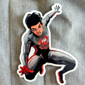 May include: A black and red superhero sticker with a black and white illustration of a young man wearing a black and red suit with a spider symbol on the chest. The superhero is in a jumping pose with one arm raised.