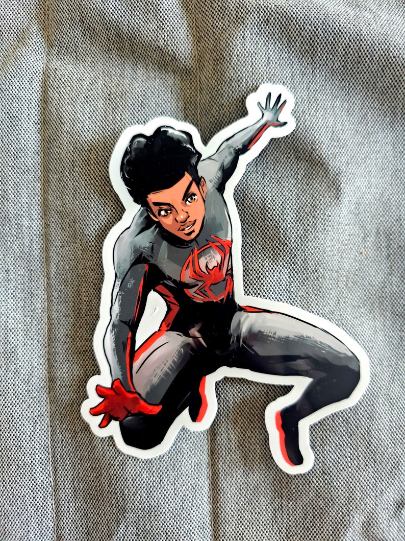 May include: A black and red superhero sticker with a black and white illustration of a young man wearing a black and red suit with a spider symbol on the chest. The superhero is in a jumping pose with one arm raised.