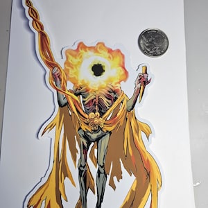 May include: A sticker featuring a skeletal figure with a flaming head and a long, twisted staff. The figure is draped in a golden cape and holds a knife. The sticker is on a white background.