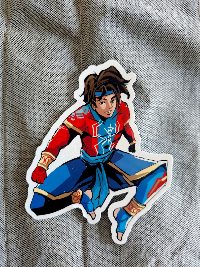 May include: A sticker of a cartoon character wearing a red and blue outfit with a gold belt. The character has brown hair and is in a jumping pose.