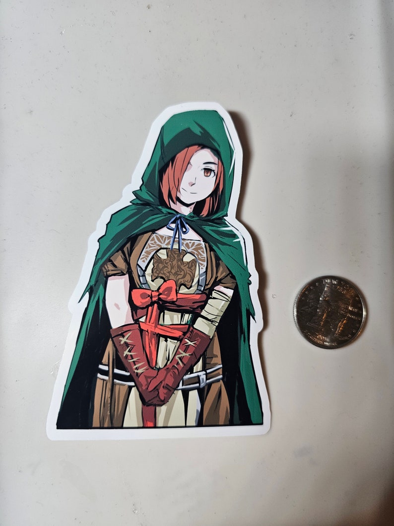 May include: A sticker featuring a cartoon illustration of a woman with red hair wearing a green hooded cloak and a brown and red outfit. She is holding her hands together in front of her.