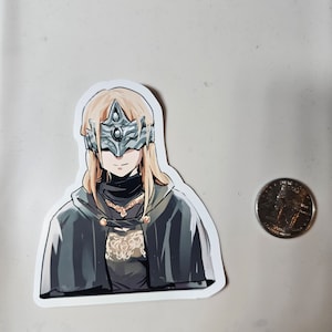 May include: A sticker featuring a character from a video game. The character is a woman with long blonde hair, wearing a dark cloak and a silver mask with a large, central gem. The sticker is on a white background.