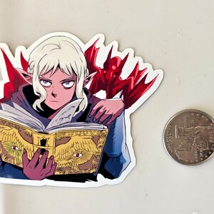 May include: A sticker featuring a white-haired elf character with purple eyes, wearing a blue robe and holding a golden book with red eyes on the cover. A red demon with wings is behind the elf.