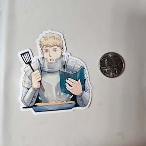 May include: A sticker featuring a cartoon man in armour, holding a spatula and a cookbook, standing in front of a pan of food. The man has blonde hair and a surprised expression. The cookbook has the word "Recipes" on the cover.