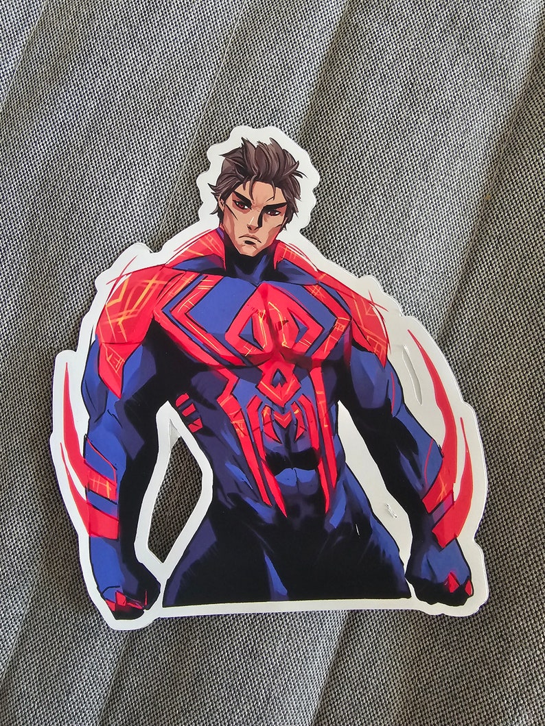 May include: A sticker featuring a superhero in a red and blue suit with a spider symbol on the chest. The superhero has a determined expression and is posed in a heroic stance.