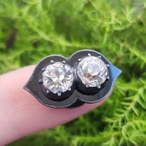 May include: A pair of black enamel earrings with two clear round stones set in the center.