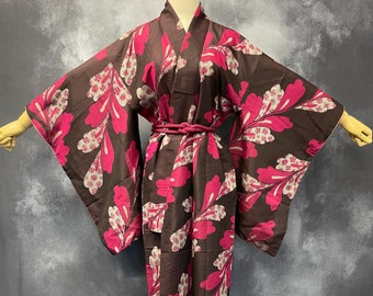 Op de afbeelding: Een bruine en roze kimono met een bloemenpatroon. De kimono is op een mannequin en heeft een bruine band om de taille geknoopt.