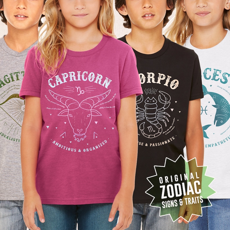 May include: Four children's t-shirts with zodiac signs and traits. The shirts are pink, black, gray, and white. The signs are Capricorn, Scorpio, Sagittarius, and Pisces.