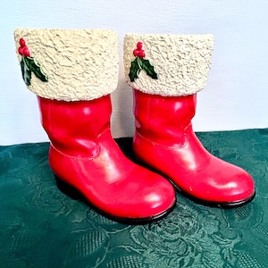 Peut inclure: Une paire de bottes décoratives rouges avec un revers crème texturé. Chaque revers est orné d'une branche de houx avec des baies rouges et des feuilles vertes. Les bottes ont une finition brillante et une semelle noire.