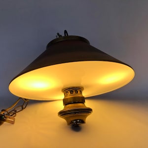 May include: A brass hanging lamp with a white and brown lampshade. The lampshade is tilted downwards and the light is on, illuminating the room.