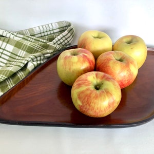May include: A wooden serving tray with a dark brown finish and a slightly curved shape. Five red and yellow apples are arranged on the tray.
