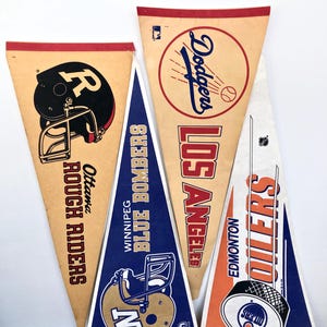 May include: Three vintage pennants, one for the Ottawa Rough Riders, one for the Winnipeg Blue Bombers, and one for the Edmonton Oilers. The pennants are all triangular and feature the team's logos and names.