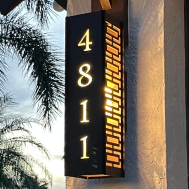 May include: Black metal house number plaque with a geometric pattern. The numbers 4811 are displayed in white on the plaque.