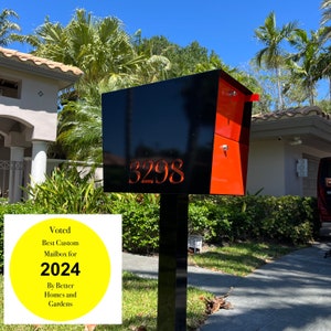 Puede incluir: Un buzón negro y rojo con el número 3298 en la parte delantera. Una pegatina circular amarilla en el poste dice "Voted Best Custom Mailbox for 2024 By Better Homes and Gardens".