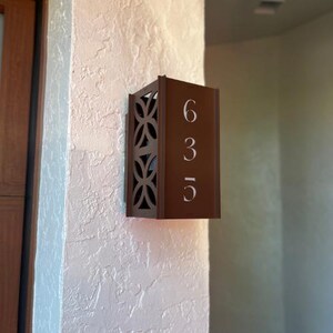 May include: A brown metal house number plaque with a decorative design and the numbers 635 in white.