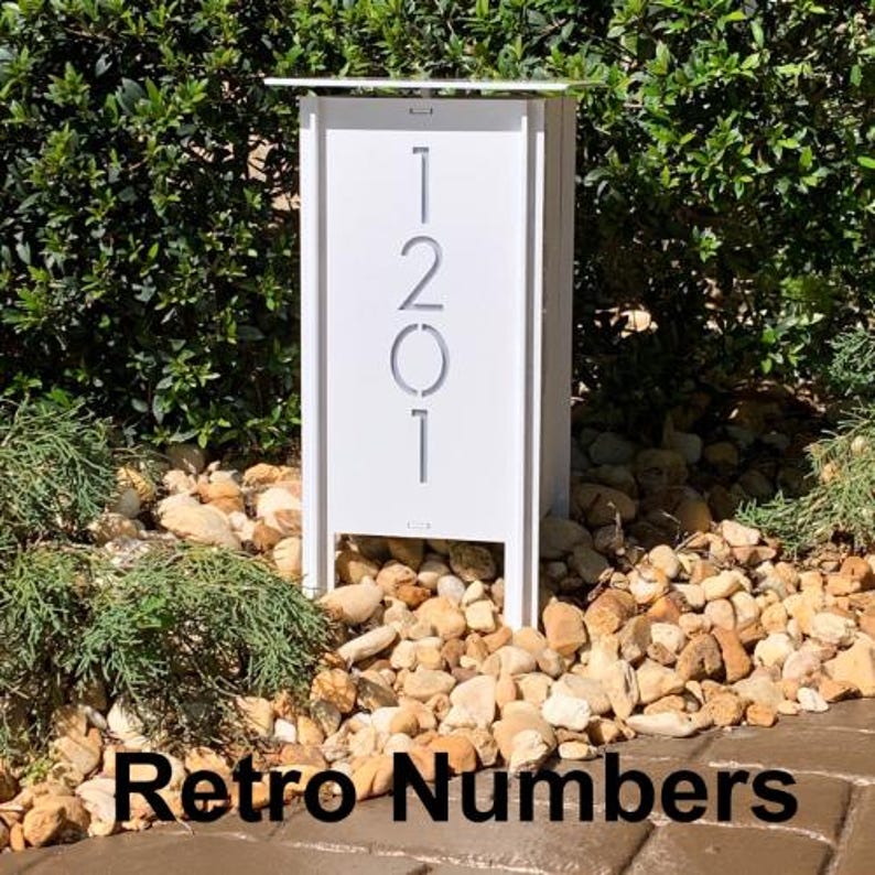 May include: White metal house number sign with the numbers 1201 cut out. The sign is mounted on a white metal post and is surrounded by small rocks.